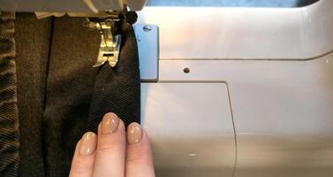 process of sewing in a sewing machine sew woman's hands manicure black textile denim jeans manufacturing close up seamstress in workshop fabric clothes making design hobby handmade working needlework photo