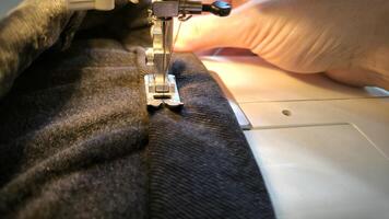 process of sewing in a sewing machine sew woman's hands manicure black textile denim jeans manufacturing close up seamstress in workshop fabric clothes making design hobby handmade working needlework photo