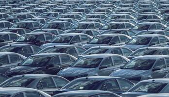 filas de un nuevo carros estacionado en un distribución centrar en un coche fábrica en un soleado día. parte superior ver a el estacionamiento. foto