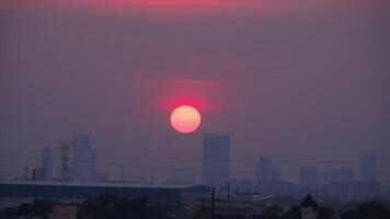 cenas do uma vermelho volta Sol pôr do sol dentro a cidade. silhuetas do cidade edifícios contra pôr do sol fundo. smog e neblina dentro a ar. de Meio Ambiente poluição video