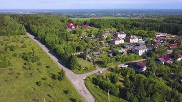 Beautiful view from the helicopter . Clip. A beautiful green summer road near the city, with small residential buildings and a beautiful landscape of forests, mountains and misty fields. video