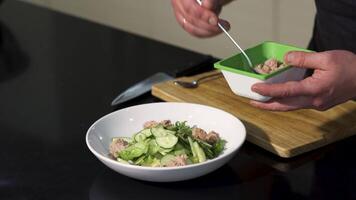 Fresh organic salad with tuna in white bowl. Art. Close up of chef hands adding fish into the green salad at the kitchen, concept of cooking food. video