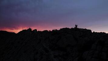 siluetas de personas haciendo yoga en montañas a amanecer. acción. turistas disfrutando ver en alto rock en el temprano mañana, turismo, de viaje y sano estilo de vida concepto. video