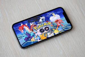 Pokemon GO mobile iOS game on iPhone 15 smartphone screen on wooden table during mobile gameplay photo