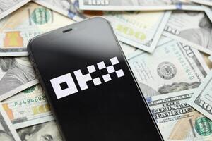 KYIV, UKRAINE - MARCH 15, 2024 OKX logo on iPhone display screen with many hundred dollar bills photo