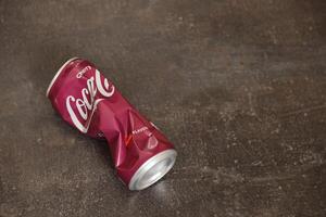 KYIV, UKRAINE - 4 MAY, 2023 Coca cola soft drink crumpled tin can with cherry flavour photo
