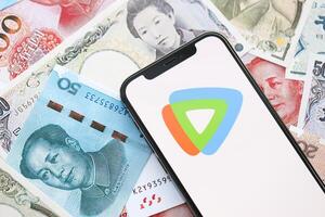 KYIV, UKRAINE - APRIL 1, 2024 Tencent WeTV icon on smartphone screen on many asian money bills photo