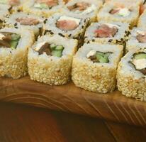 Close-up of a lot of sushi rolls with different fillings lie on a wooden surface. Macro shot of cooked classic Japanese food with a copy space photo