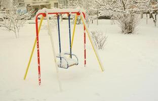 Children's swing, covered with a thick layer of snow after a heavy snowfall photo