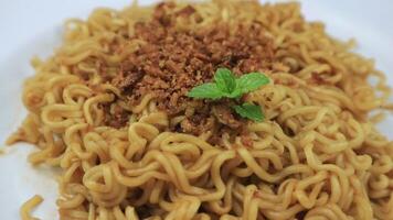 instant fried noodles sprinkled with spices and mint leaves on top, served on a white plate. Rotating display video