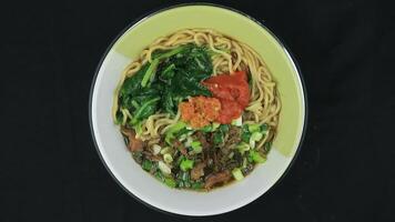 Mie Ayam or Chicken noodle, Popular Indonesian Street Food served in a bowl with sauce and chili sauce. Top View, rotary display, video