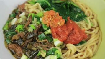 Mie Ayam or Chicken noodle, Popular Indonesian Street Food served in a bowl with sauce and chili sauce. Top View, rotary display, video