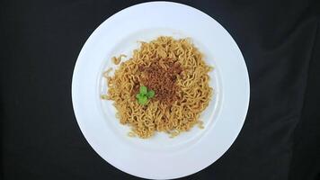 instant fried noodles sprinkled with spices and mint leaves on top, served on a white plate. Rotating display video