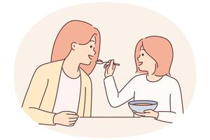 Little girl feeds mother with spoon during breakfast sitting at kitchen table spending time together vector