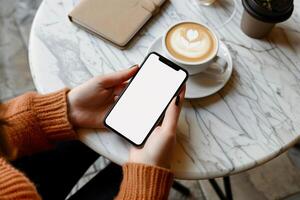 Hands holding phone with white mockup screen against coffee table backdrop photo