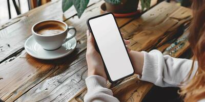 Hands holding phone with white mockup screen against coffee table backdrop photo