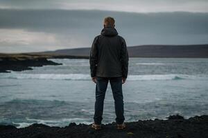 man standing on the edge of a cliff looking at the ocean photo