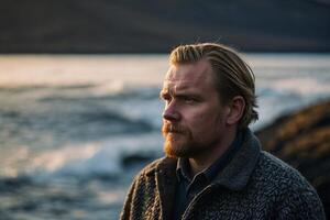 a man with a beard and a sweater standing near the ocean photo