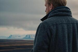 man standing on the edge of the cliff looking at the ocean photo