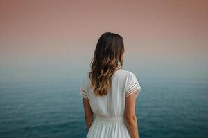 un mujer en un blanco vestir en pie en un muelle mirando fuera a el Oceano foto