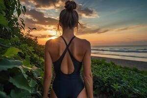 un mujer en un uno pedazo traje de baño soportes en el playa a puesta de sol foto