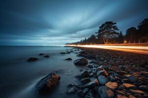 a long exposure photograph of a road and rocks by the water photo