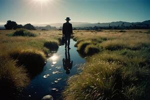 a man in a hat standing in a stream with grass photo