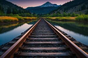 railroad tracks leading to a mountain with a river in the background photo