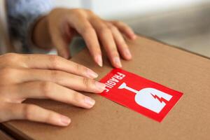 Woman Hand Sticking Fragile Mark Sticker to Parcel. photo