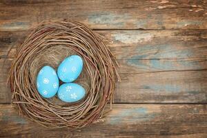 Blue Easter eggs in bird's nest on wooden background - top view photo