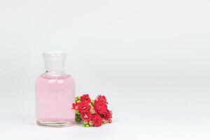 transparente botella con aromático rosado líquido y rojo flores foto