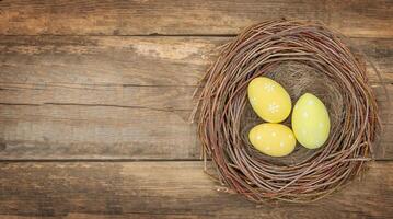 Three yellow Easter eggs in bird's nest on wooden background - top view photo
