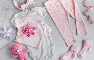 Set of baby bodysuits, pants, socks and knitted toy on grey background. photo