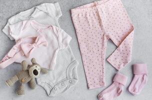 Set of baby bodysuits, pants, socks and knitted toy on grey background. photo