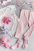 Set of baby bodysuits, pants, socks and knitted toy on grey background. photo