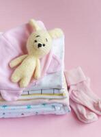 Baby knitted toy of bunny next to a stack rompers for kids photo