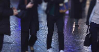 Walking people at the crossing in Shinjuku Tokyo rainy day at night handheld video