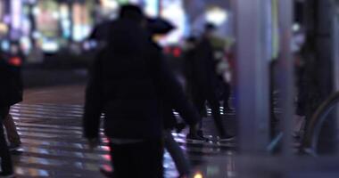 Walking people at the crossing in Shinjuku Tokyo rainy day at night handheld video