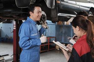 asiático masculino profesional automotor ingeniero supervisor describe coche rueda y suspensión reparar trabajo con mecánico trabajador personal equipo en reparar Servicio cochera, especialista ocupaciones en auto industria. foto