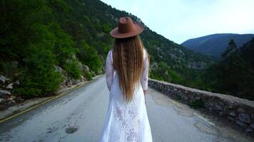 hembra viajero en marrón sombrero y blanco vestir mirando a increíble montañas y bosque, pasión de viajar viaje concepto, atmosférico épico momento video