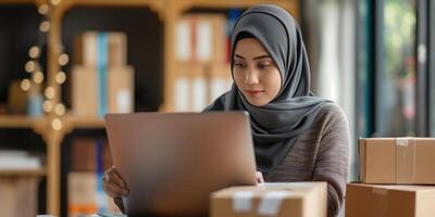 A young Muslim woman in a hijab, business woman surrounded by boxes, working on a laptop. Small business, delivery, businesswoman. Proud business owner. Bokeh effect. photo