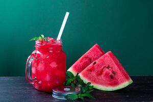 Cold watermelon smoothie and pieces of refreshment watermelon on dark background. Fresh summer drink. photo