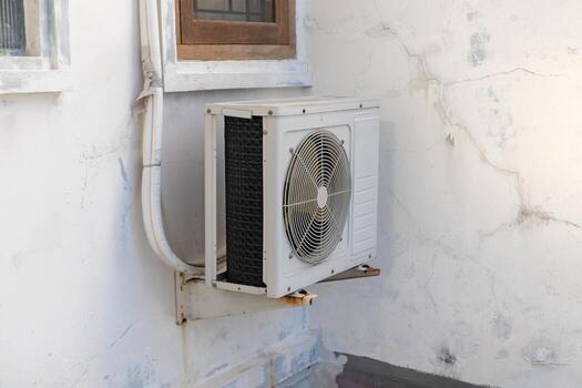 Condenser unit or compressor of air conditioner hanging on a white wall outside home photo