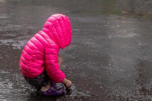 An Asian little girl wearing a pink jacket and playing in the rain on the street photo