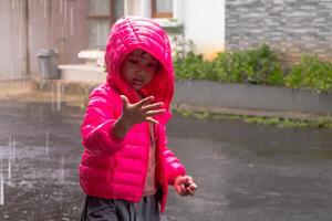 An Asian little girl wearing a pink jacket and playing in the rain in front of the house photo