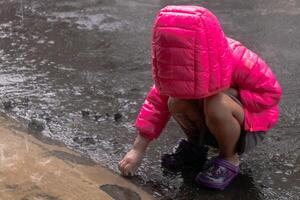 A little Asian girl in a crouching position wearing a pink jacket and playing in the rain photo