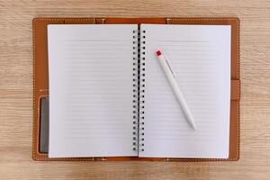 A open notebook with a leather cover and a pen on the wooden table photo