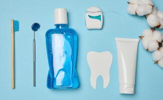 Mouthwash, toothpaste tube, dental floss and medical mirror on a blue background photo