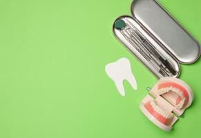 Metal dentist tools, plastic jaw model with white teeth on a green background photo