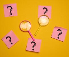 Drawn question marks on stickers and a magnifying glass, yellow background. photo